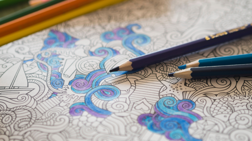 A photo of a coloring page with detailed geometric designs. There are blue and purple sections colored in and blue and purple pencils are laying across the page.