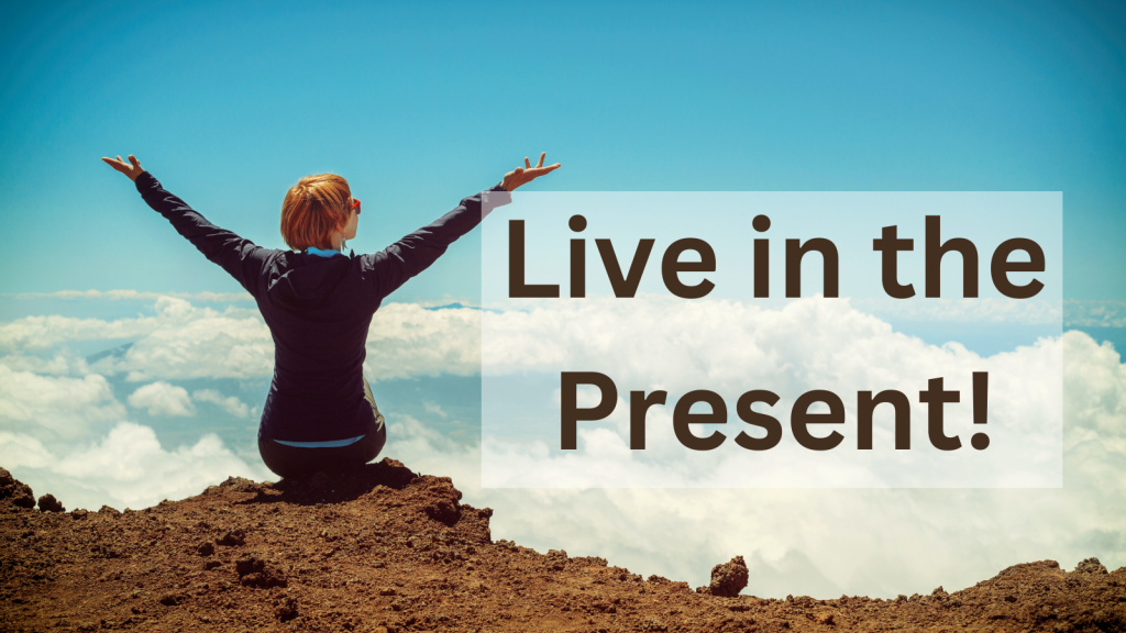 Woman sitting on top of mountain looking into the sky with her arms raised into a "V" over her head with the words, "Live in the Present!" over the sky.