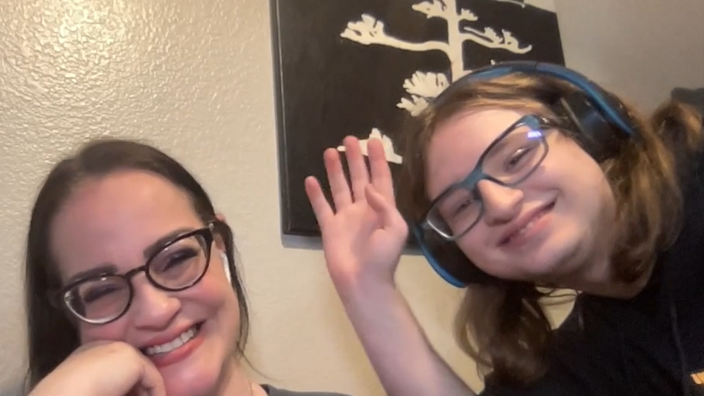 A screenshot from the interview with Stacey Short on the left smiling at the camera and her son, Bryce, on the right and waving at the camera. Stacey and Bryce are both wearing glasses and have brown hair. Bryce is also wearing headphones.