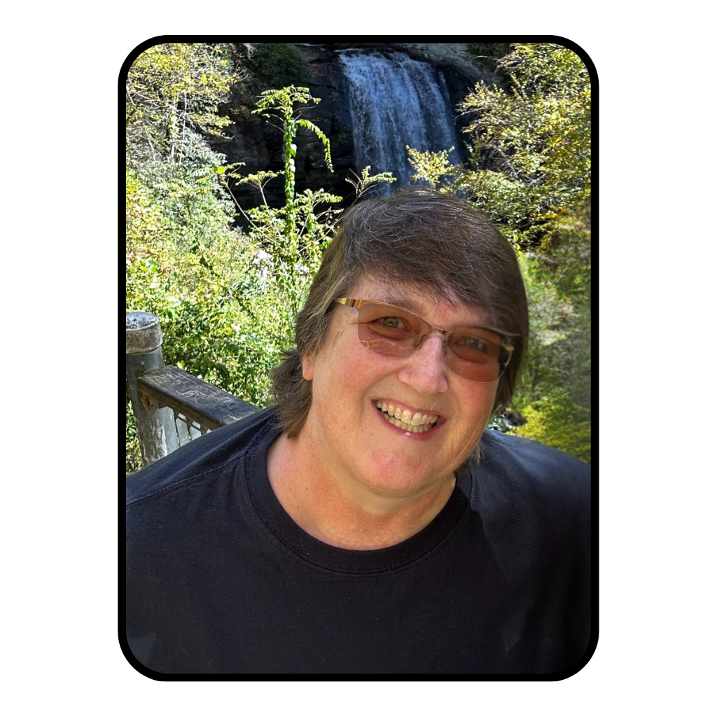 A woman with short brown hair and wearing glasses is standing outside with a waterfall in the background behind her.