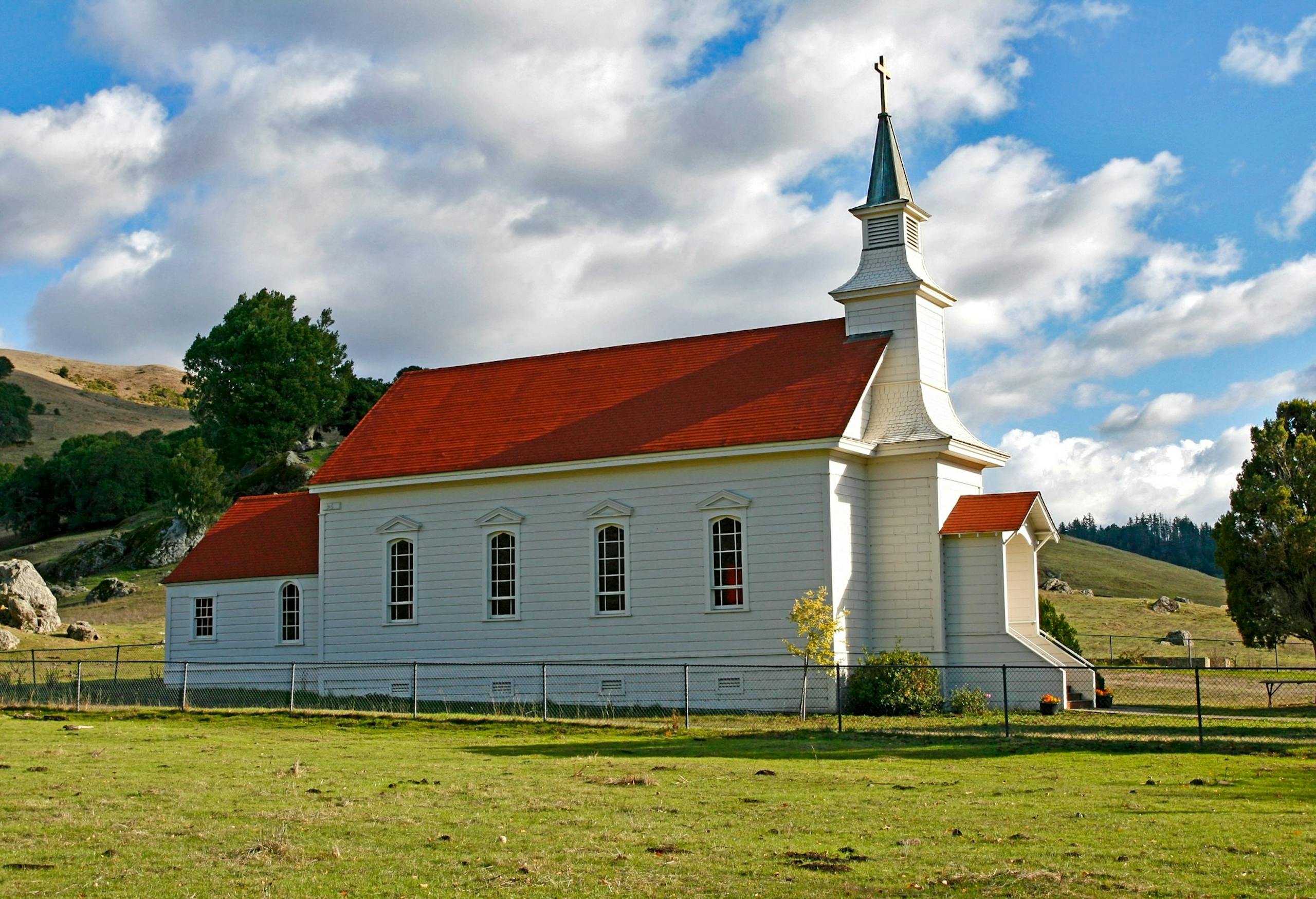 Charming rural church with red roof and steeple against a picturesque countryside backdrop.