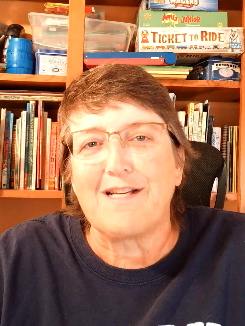 A photo of a woman with short hair and glasses in front of a bookcase.