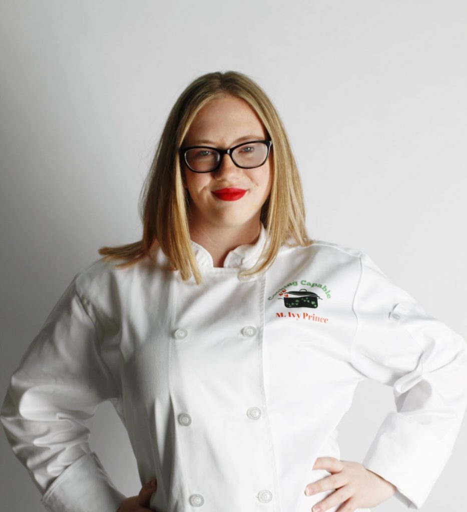 A teen girl with blond hair and glasses wearing a chef's uniform.